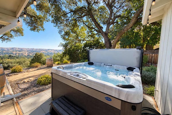 Hot tub on covered patio with valley and oak tree views, string lights overhead