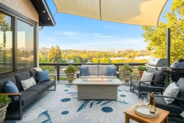 Sunroom with beige sectional sofa, wooden ceiling, and large windows overlooking rolling hills and countryside.